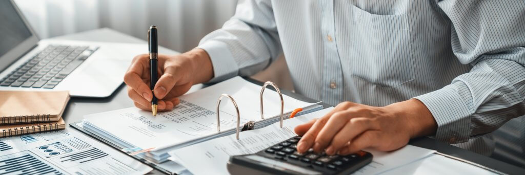 Corporate auditor calculating budget with calculator on his office desk. Insight